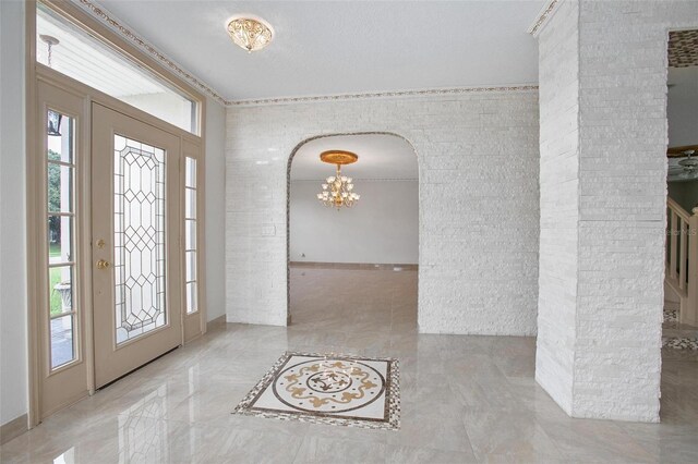 foyer with a chandelier, crown molding, and ornate columns