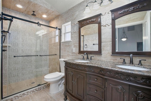 bathroom with tile walls, tile patterned flooring, walk in shower, vanity, and toilet