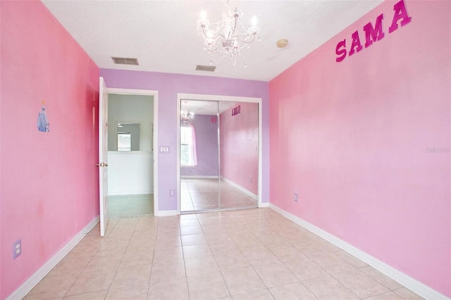 unfurnished bedroom with an inviting chandelier, a closet, light tile patterned floors, and a textured ceiling