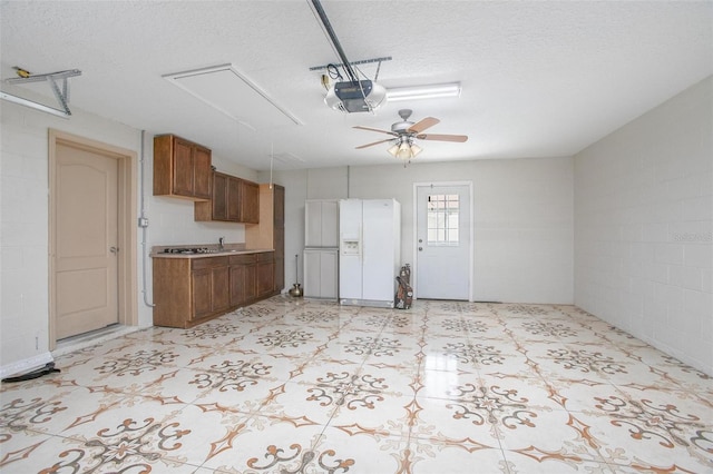 garage featuring ceiling fan, white refrigerator with ice dispenser, and a garage door opener