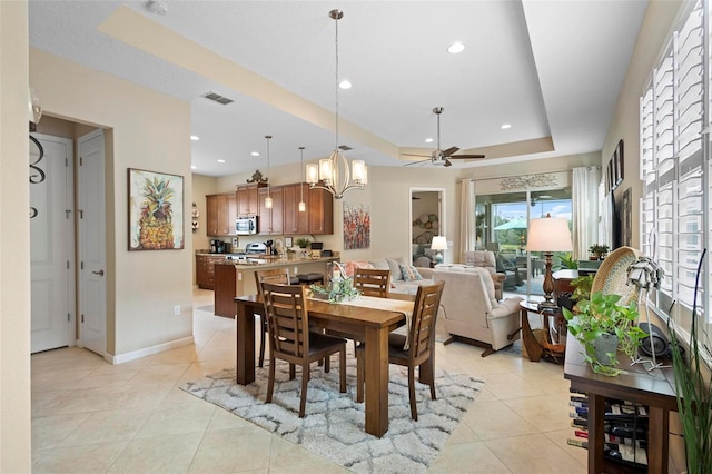 tiled dining room featuring ceiling fan with notable chandelier and a tray ceiling