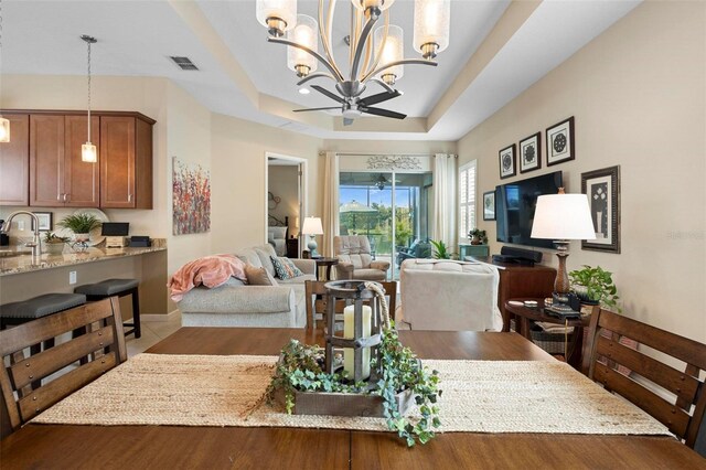 dining space with ceiling fan with notable chandelier, sink, and a raised ceiling