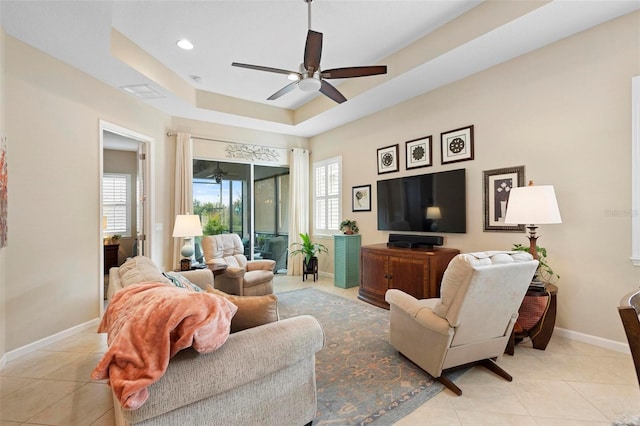 tiled living room with a raised ceiling and ceiling fan