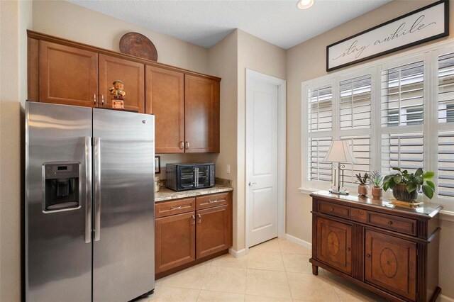 kitchen with light tile patterned floors, light stone countertops, and stainless steel fridge with ice dispenser