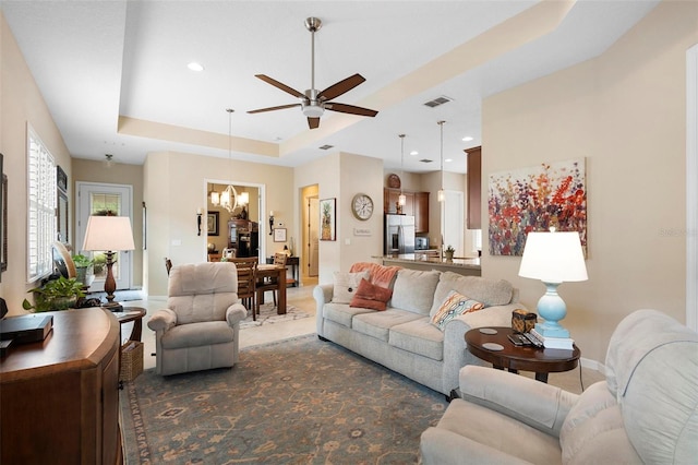 living room featuring ceiling fan with notable chandelier and a raised ceiling