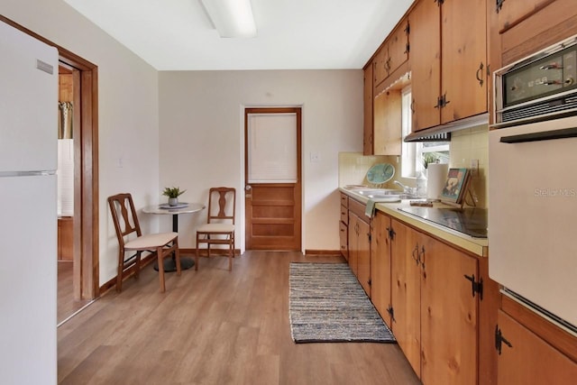 kitchen with sink, light hardwood / wood-style floors, white appliances, and tasteful backsplash