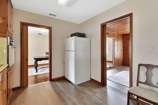 kitchen with wood-type flooring, oven, wood walls, and white refrigerator