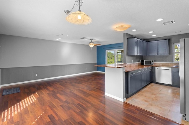 kitchen featuring kitchen peninsula, stainless steel appliances, ceiling fan, hardwood / wood-style flooring, and hanging light fixtures