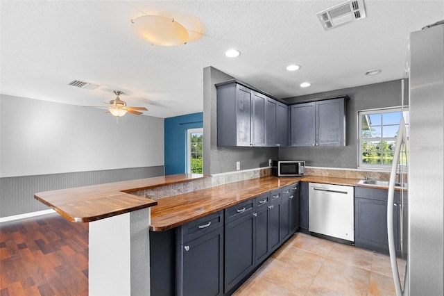 kitchen with wood counters, ceiling fan, a textured ceiling, kitchen peninsula, and stainless steel appliances