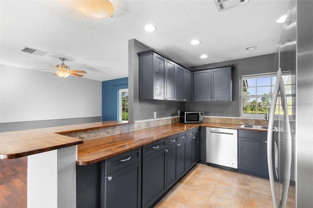 kitchen featuring kitchen peninsula, appliances with stainless steel finishes, a kitchen bar, a textured ceiling, and butcher block countertops