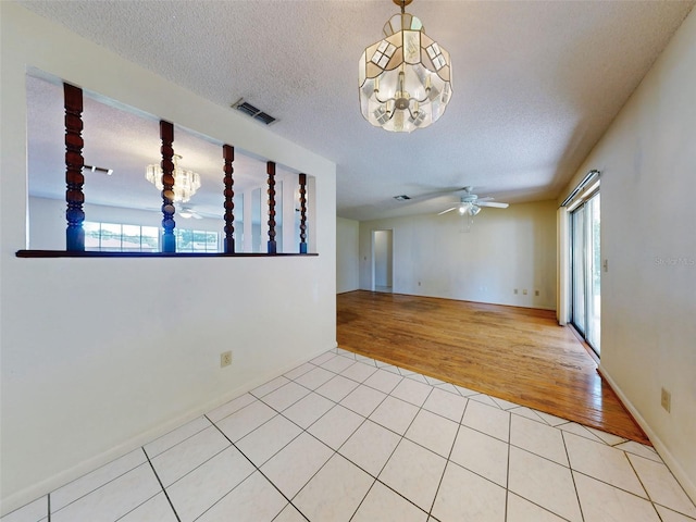 empty room featuring a textured ceiling, ceiling fan with notable chandelier, and light hardwood / wood-style flooring