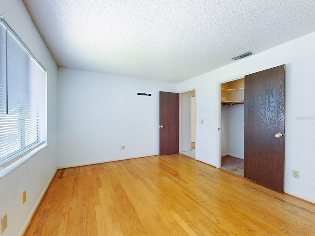 unfurnished bedroom featuring wood-type flooring, a textured ceiling, a closet, and a walk in closet