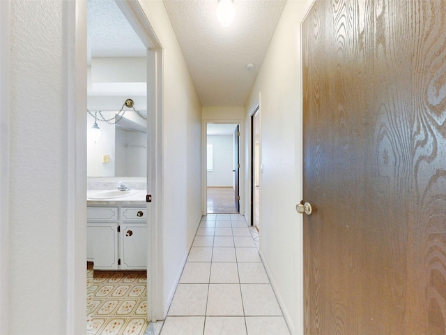 hallway with a textured ceiling, sink, and light tile patterned flooring