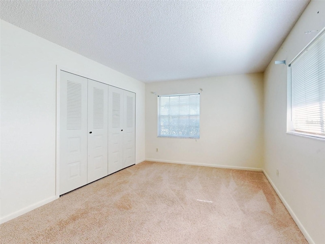 unfurnished bedroom featuring a closet, multiple windows, light colored carpet, and a textured ceiling