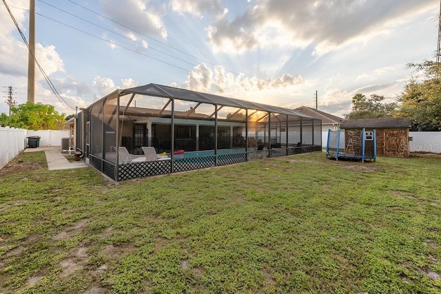 back of house with a lanai, a lawn, a shed, a fenced in pool, and central AC