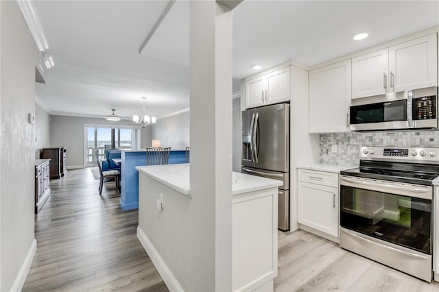 kitchen with appliances with stainless steel finishes, light hardwood / wood-style floors, white cabinets, ornamental molding, and a chandelier