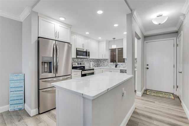 kitchen with appliances with stainless steel finishes, light stone counters, white cabinets, pendant lighting, and light wood-type flooring