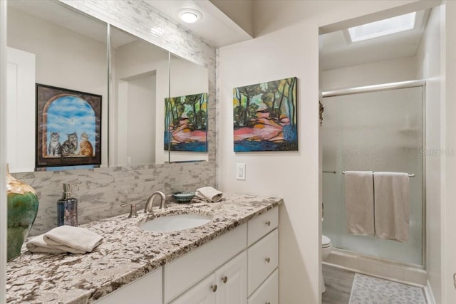 bathroom with decorative backsplash, a skylight, walk in shower, vanity, and toilet