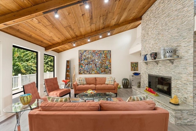 living room featuring wooden ceiling, a stone fireplace, rail lighting, vaulted ceiling with beams, and light hardwood / wood-style floors