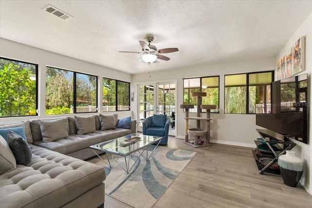 living room with ceiling fan, a healthy amount of sunlight, light wood-type flooring, and a textured ceiling