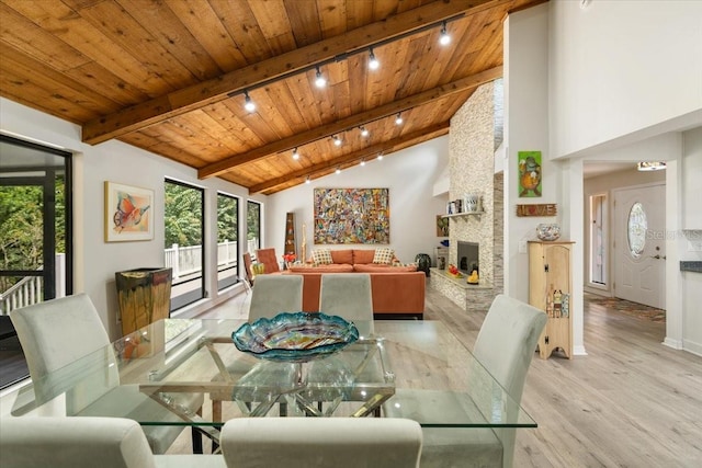 dining space with light wood-type flooring, a fireplace, wood ceiling, high vaulted ceiling, and beamed ceiling