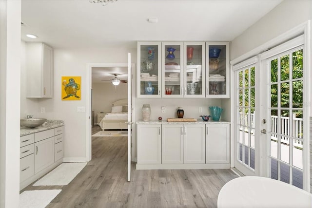 kitchen with white cabinets, light hardwood / wood-style floors, light stone counters, and french doors