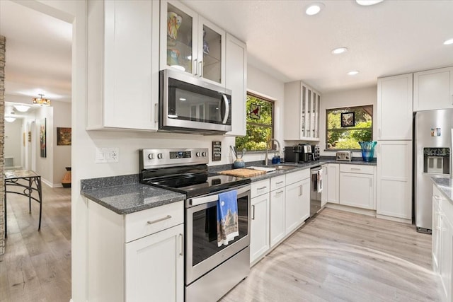 kitchen with light wood finished floors, glass insert cabinets, appliances with stainless steel finishes, white cabinetry, and a sink