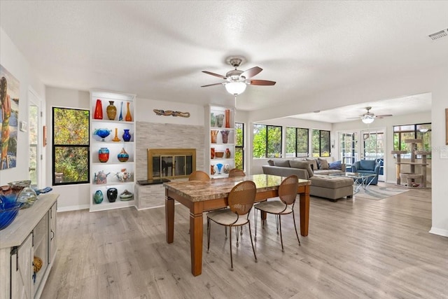 dining area featuring visible vents, light wood-style flooring, a glass covered fireplace, a textured ceiling, and baseboards