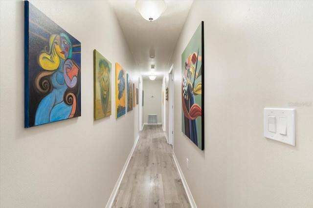 hall with light wood-style flooring, visible vents, and baseboards