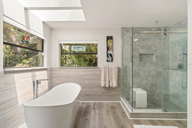 bathroom featuring wood finished floors, a stall shower, a freestanding tub, and tile walls