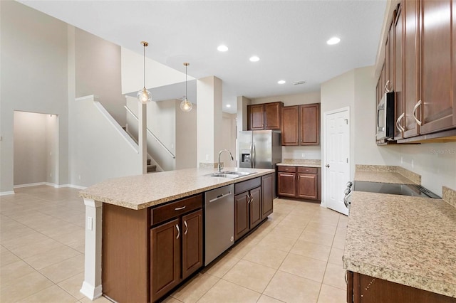 kitchen featuring stainless steel appliances, light tile patterned flooring, sink, decorative light fixtures, and a kitchen island with sink