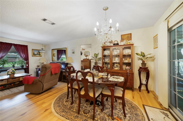 dining space featuring light wood-type flooring, a textured ceiling, and an inviting chandelier