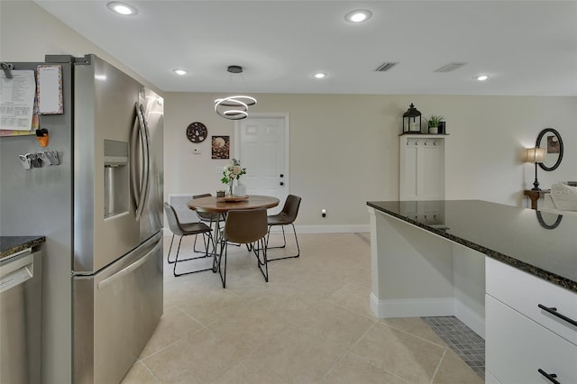 kitchen with dark stone countertops, white cabinets, light tile patterned floors, pendant lighting, and stainless steel appliances