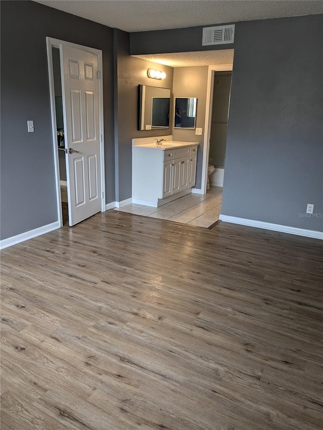 unfurnished living room featuring a textured ceiling, light hardwood / wood-style flooring, and sink