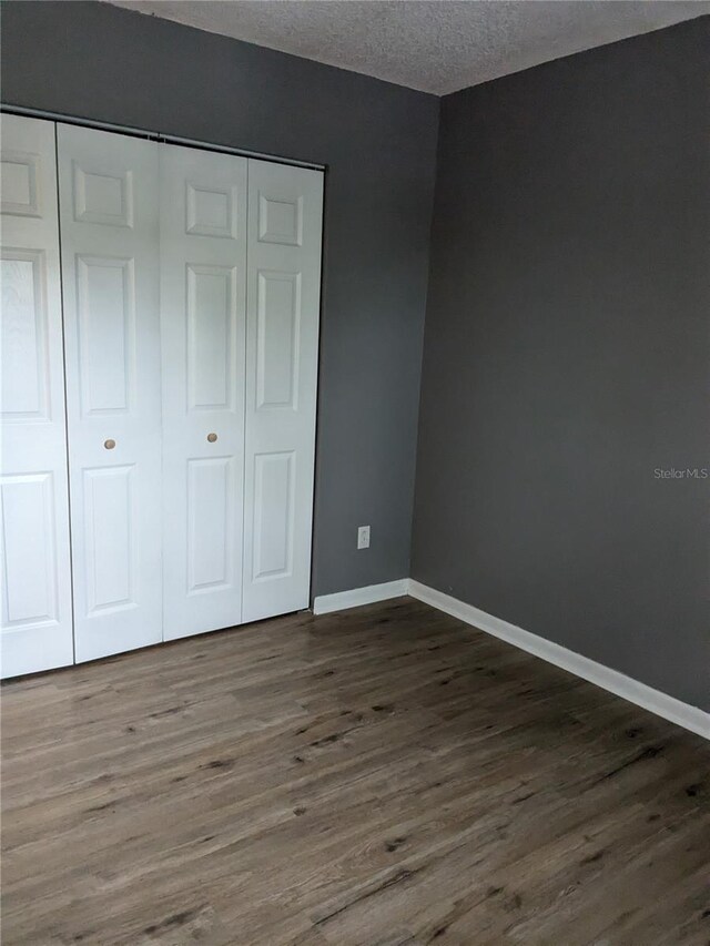 unfurnished bedroom with a textured ceiling, dark wood-type flooring, and a closet