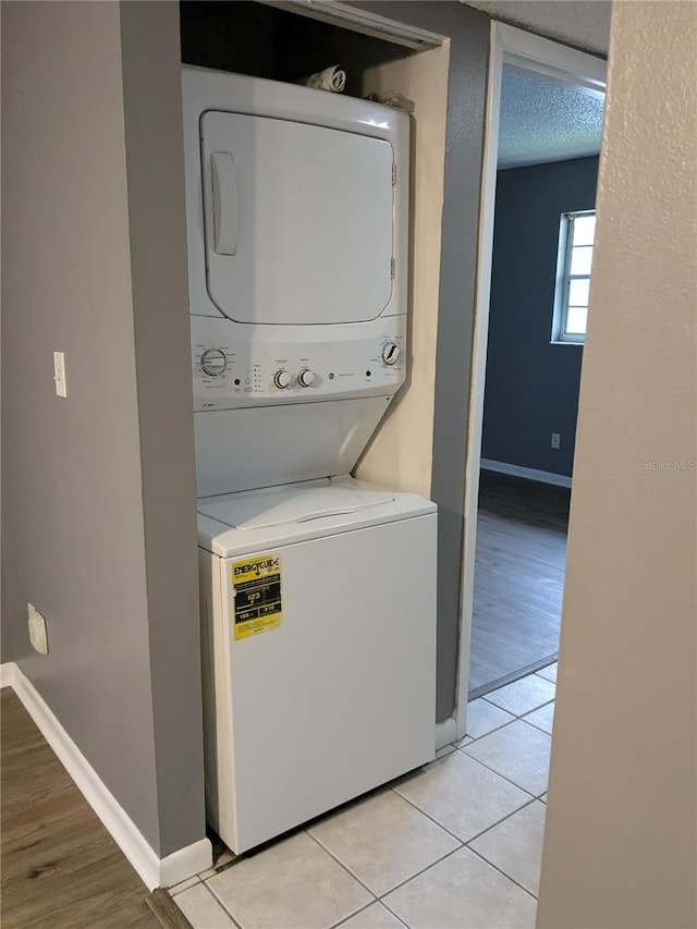 laundry area with stacked washer and dryer, a textured ceiling, and light tile patterned floors