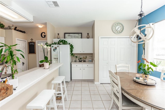 kitchen featuring white fridge with ice dispenser, white cabinetry, light tile patterned floors, and decorative light fixtures