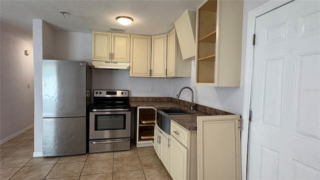 kitchen with appliances with stainless steel finishes, light tile patterned flooring, cream cabinets, and sink