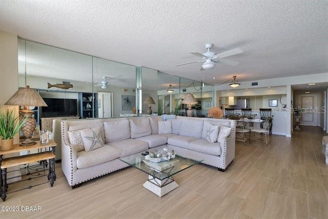 living room featuring light wood-type flooring, a textured ceiling, and ceiling fan