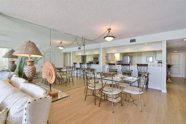 dining room with light wood-type flooring and a textured ceiling