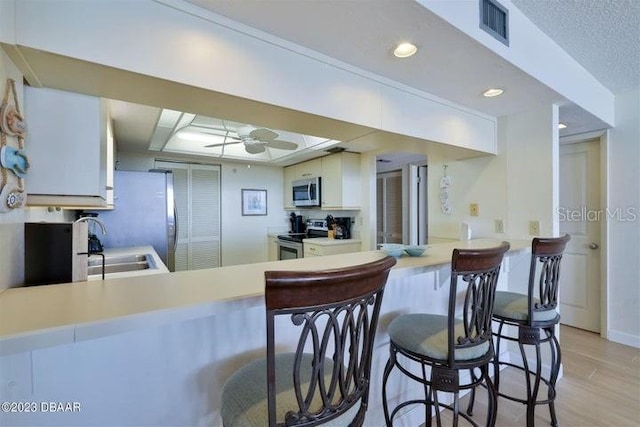 kitchen with ceiling fan, kitchen peninsula, light hardwood / wood-style flooring, white cabinetry, and stainless steel appliances