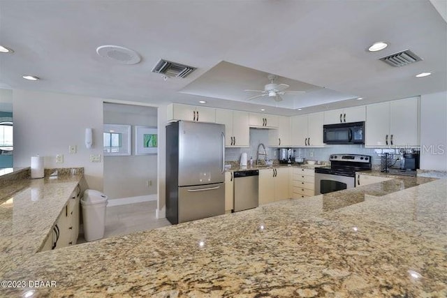 kitchen with white cabinets, appliances with stainless steel finishes, kitchen peninsula, and a tray ceiling