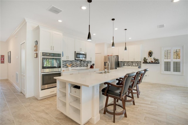 kitchen with pendant lighting, appliances with stainless steel finishes, an island with sink, and white cabinets