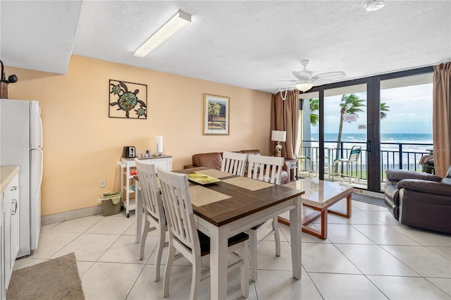 dining area featuring ceiling fan, expansive windows, light tile patterned flooring, a textured ceiling, and a water view