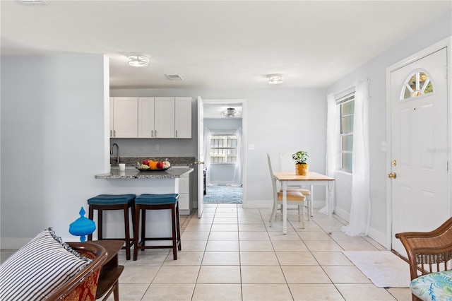 kitchen with white cabinetry, light tile patterned flooring, stone counters, and a healthy amount of sunlight