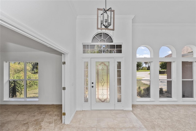 carpeted entrance foyer featuring a wealth of natural light, a chandelier, a high ceiling, and ornamental molding