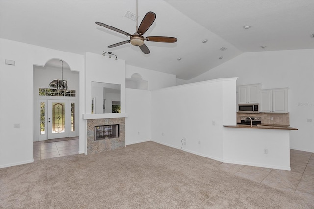 unfurnished living room featuring a tile fireplace, light colored carpet, high vaulted ceiling, and ceiling fan