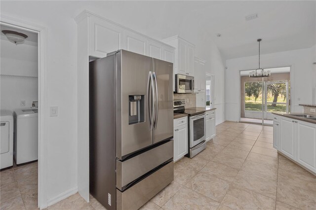 kitchen with stainless steel appliances, pendant lighting, white cabinets, washing machine and dryer, and a chandelier