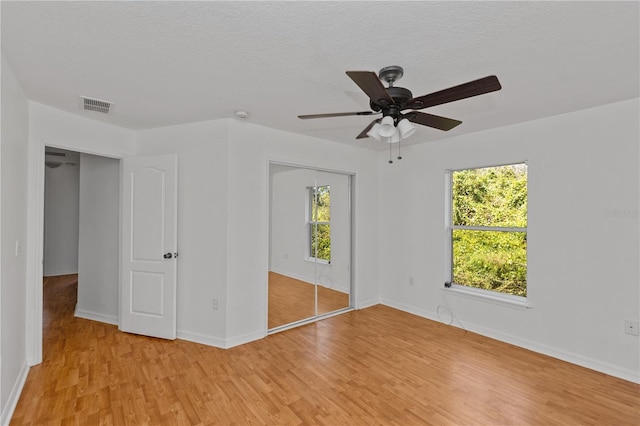 unfurnished bedroom with multiple windows, light wood-type flooring, a closet, and ceiling fan