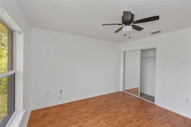 unfurnished bedroom with multiple windows, ceiling fan, a closet, and wood-type flooring